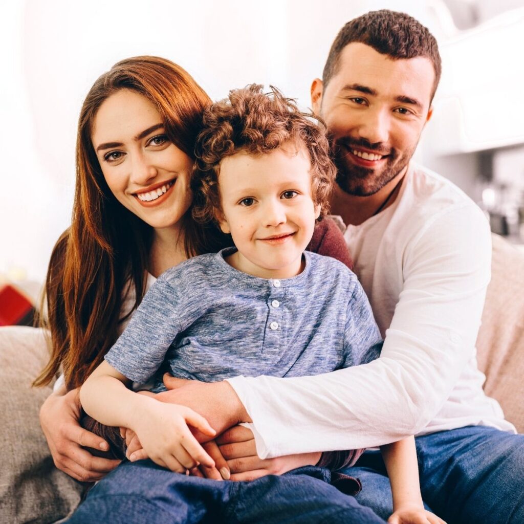 A smiling woman, a man, and a young boy sit closely together on a couch, looking happy and relaxed in a bright, cozy room—enjoying the comfort of their pest-free home thanks to local pest control.