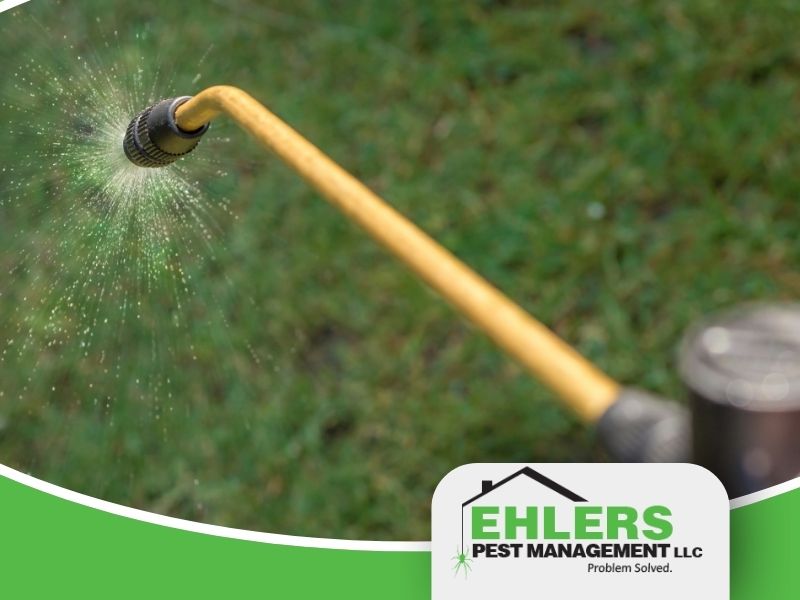 Close-up of a yellow spray nozzle releasing mist, with green grass in the background and an Ehlers Pest Management LLC logo in the lower right corner, highlighting professional pest management solutions.