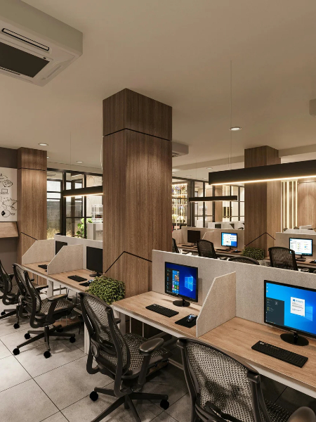 Open-plan office with rows of wooden desks, ergonomic chairs, and computer monitors separated by grey privacy partitions.